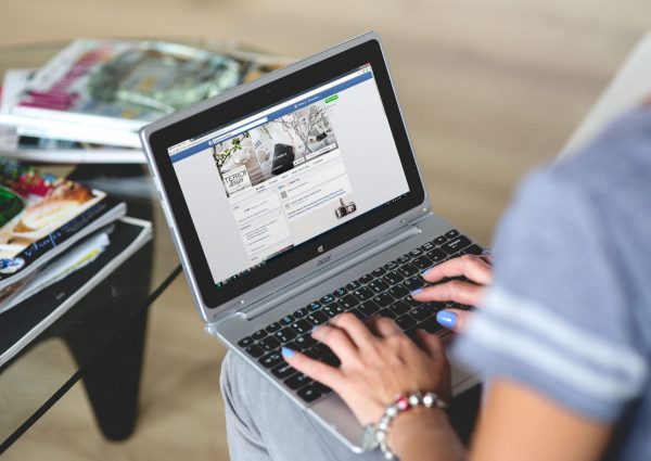 A woman typing on a laptop with social media on the screen, indoors setting.